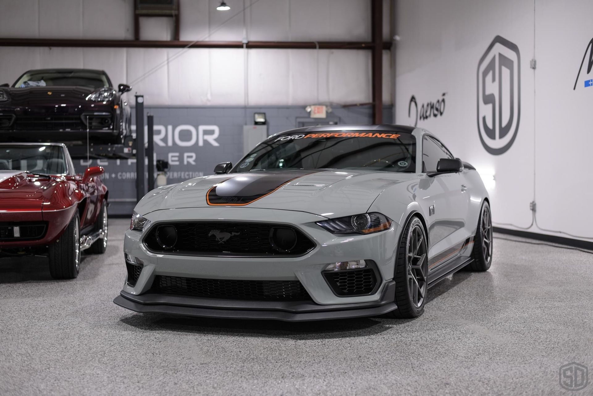 A gray mustang is parked in a garage next to a red corvette.