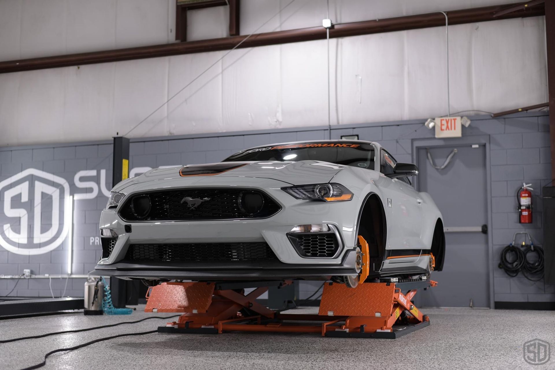 A white mustang is sitting on a lift in a garage.