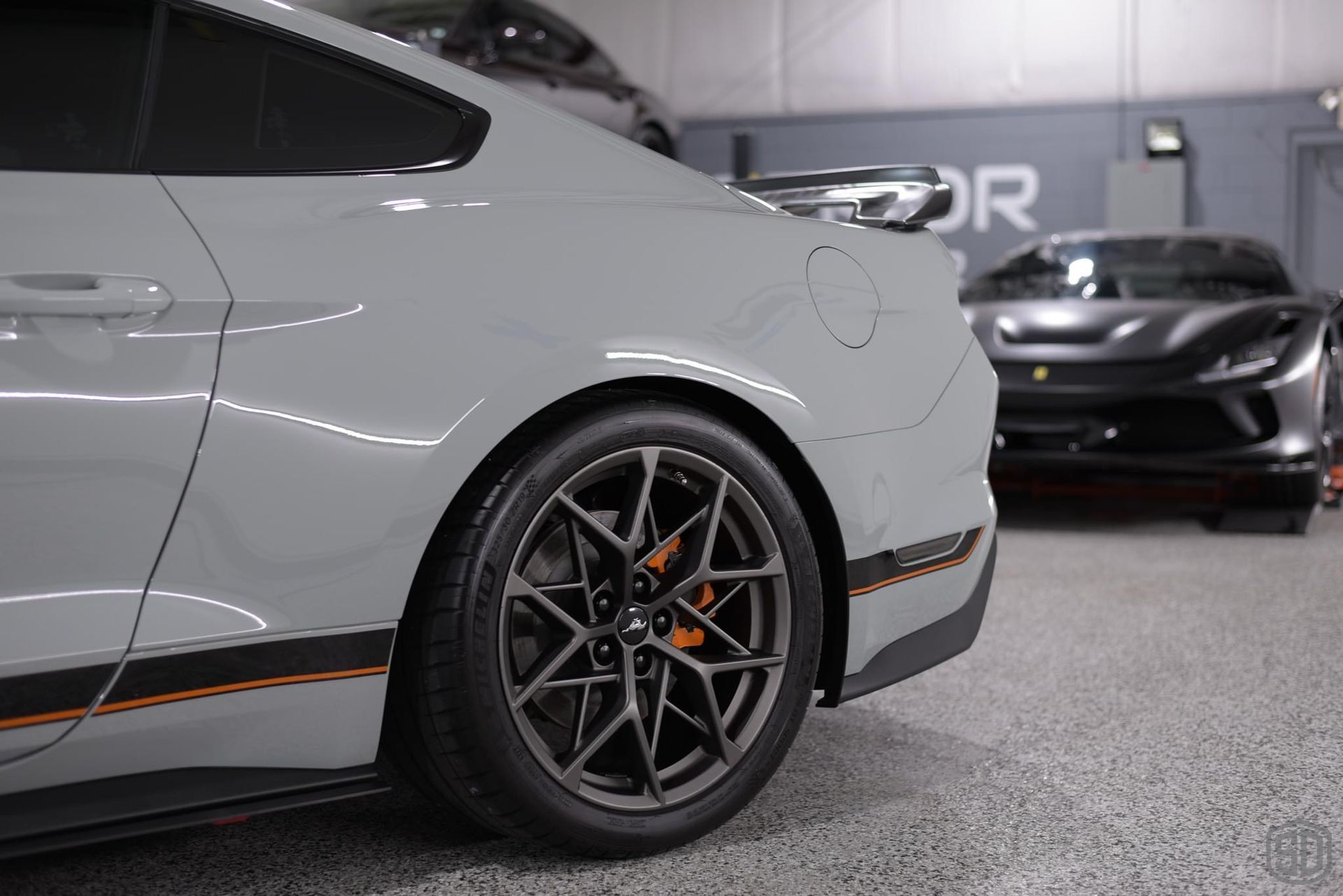 A gray mustang is parked in a garage next to a black car.
