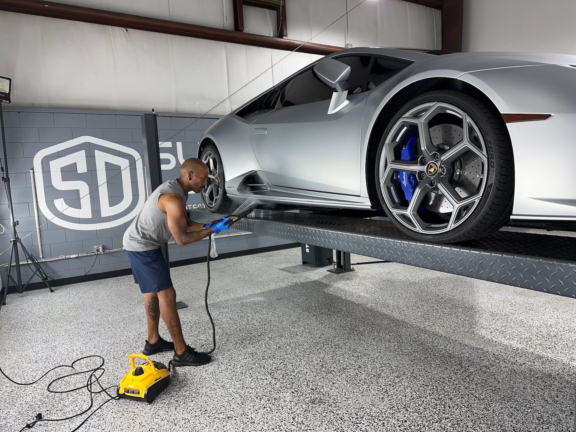 A man is polishing a silver sports car in a garage.