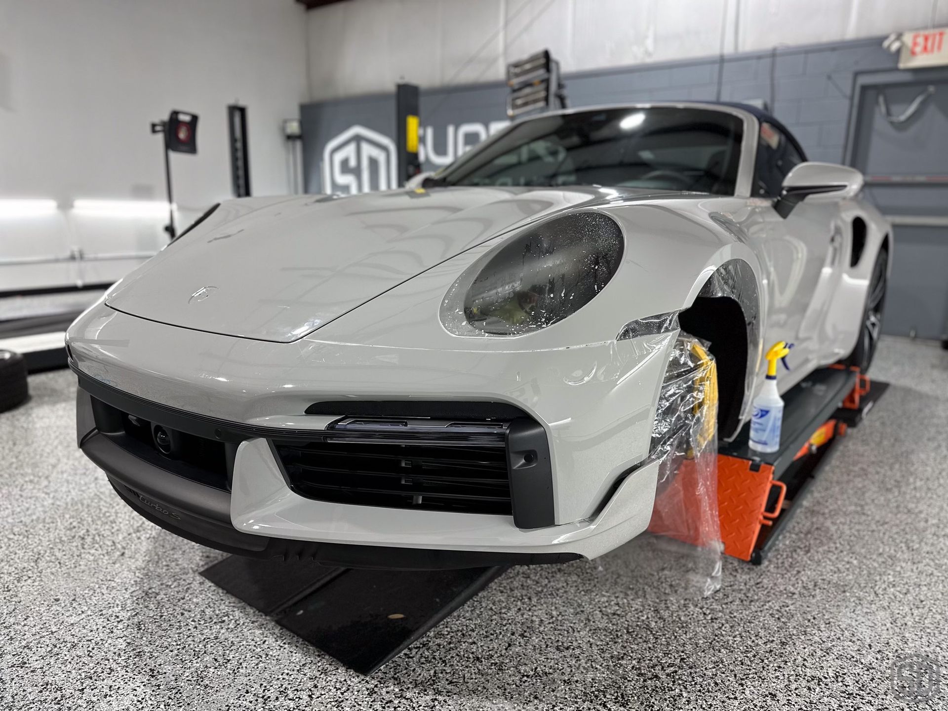 A porsche 911 turbo s is sitting on a lift in a garage.
