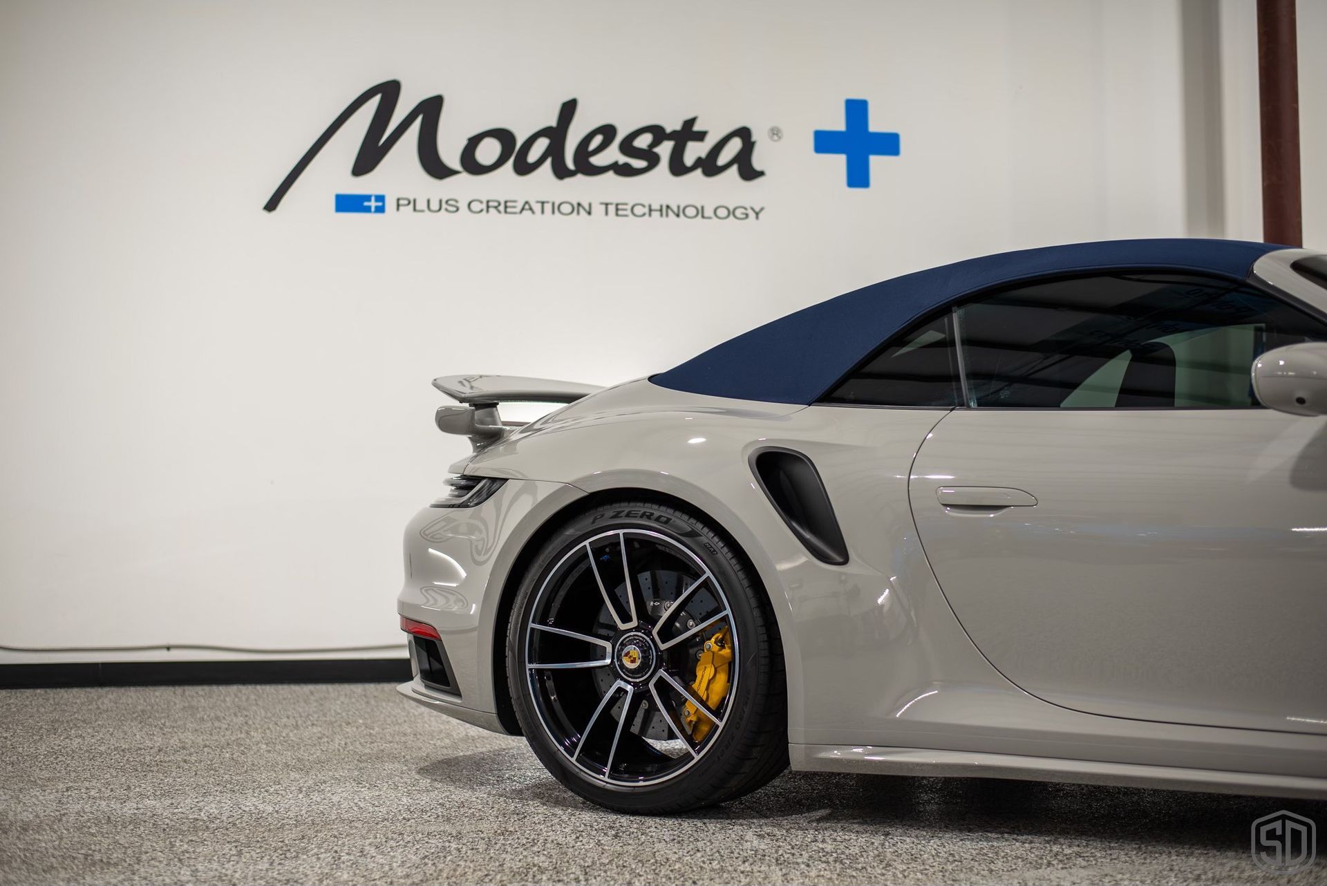 A gray sports car with a blue top is parked in a garage.