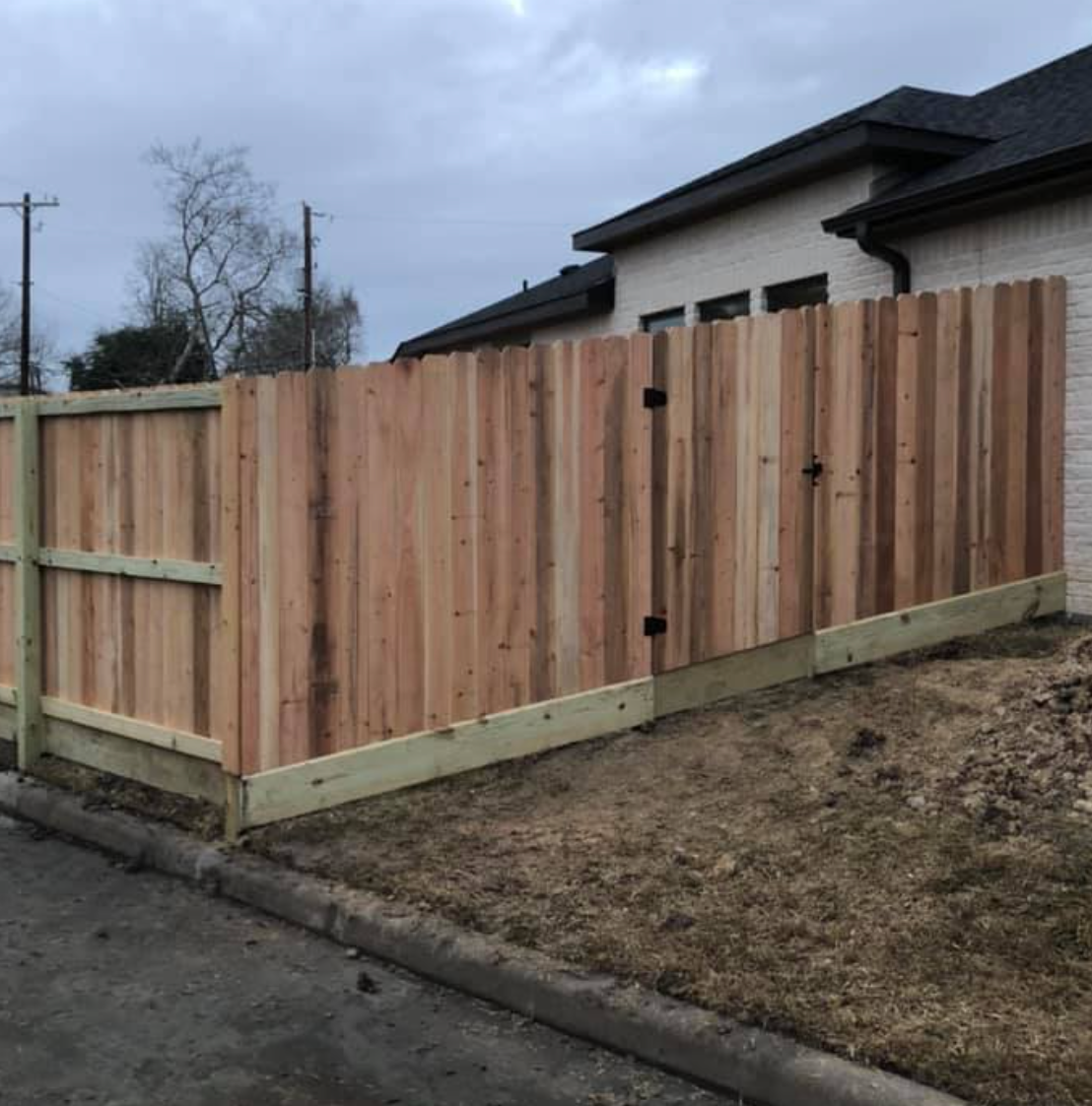 Wooden fence in front of a light brick house; cloudy sky.