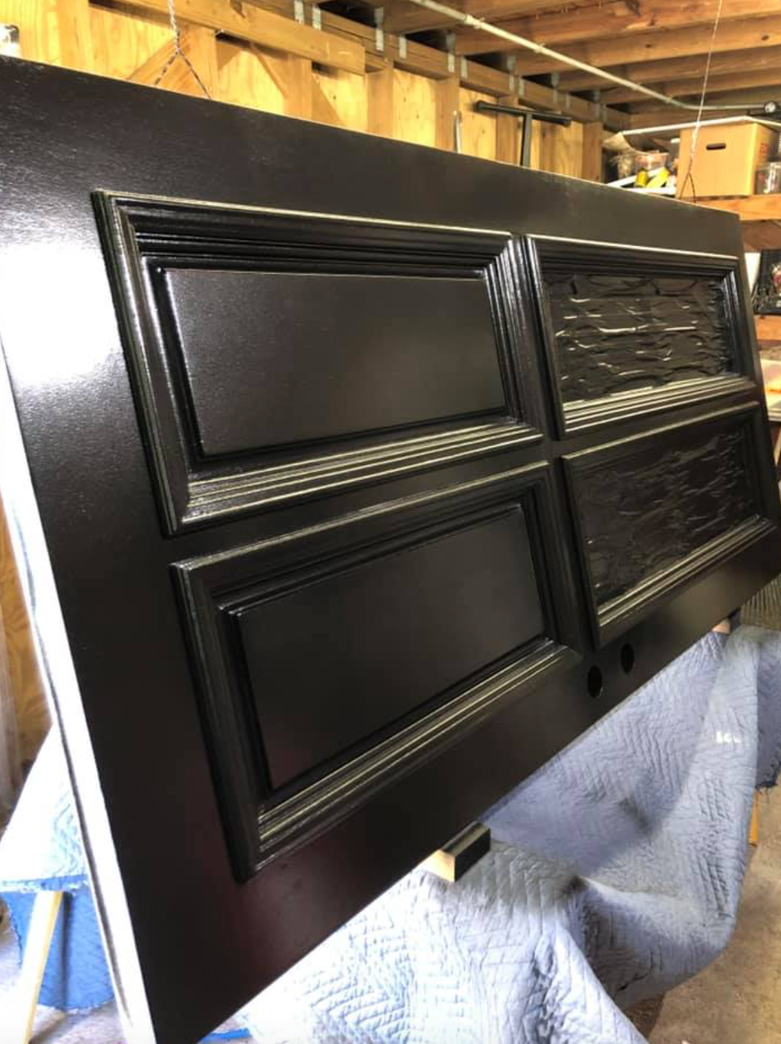 Black door with four panels; one panel textured, the rest smooth, displayed on a workbench.