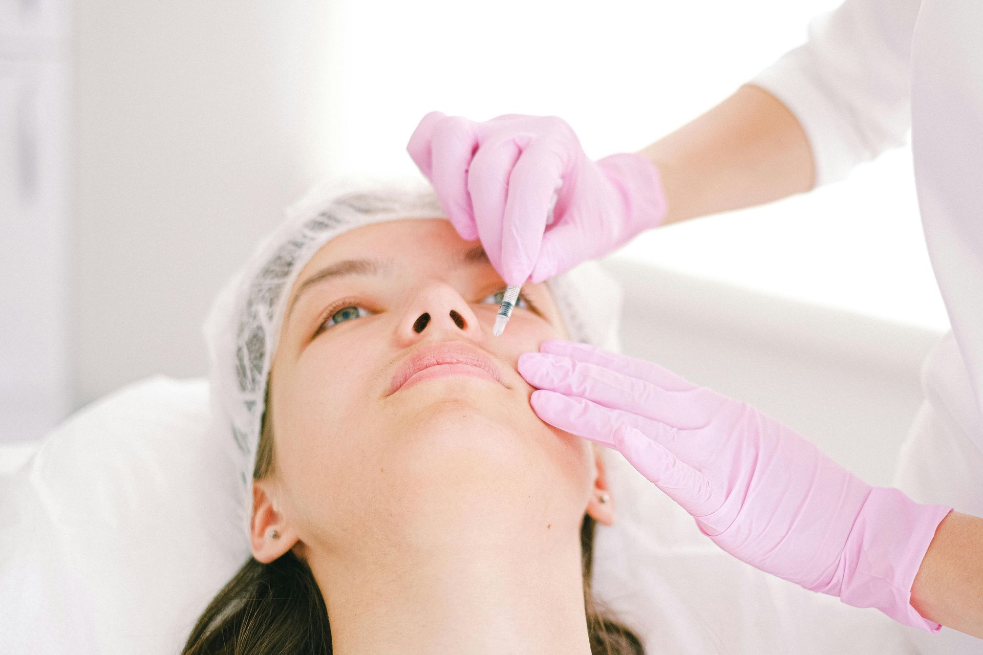 Woman receiving lip filler injection, with provider wearing pink gloves in a medical setting.