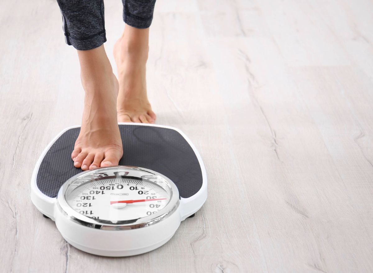 Person's foot on a scale on a wood floor; focused on weight measurement.