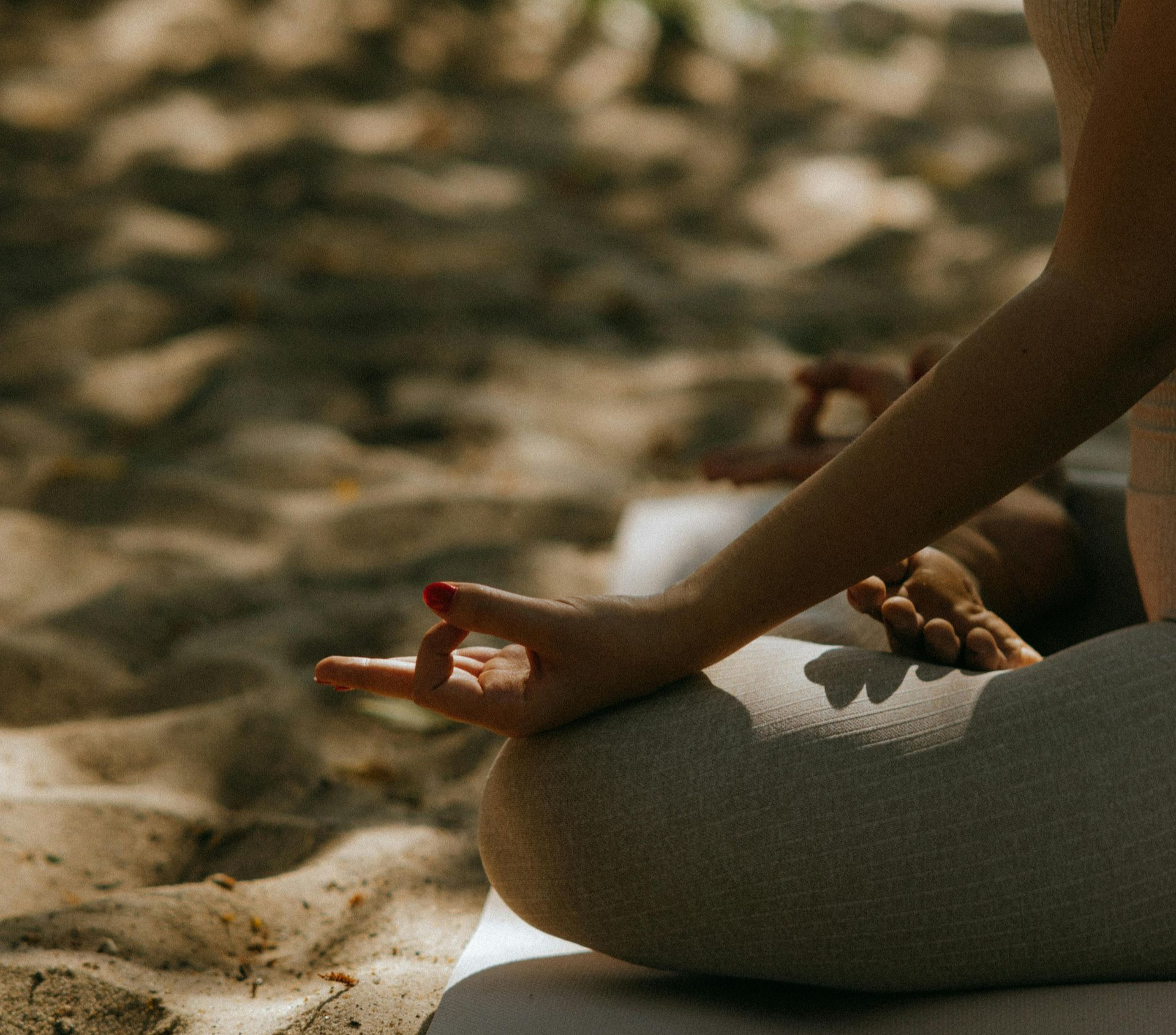 Person in lotus position, hand in mudra, meditating on a beach.