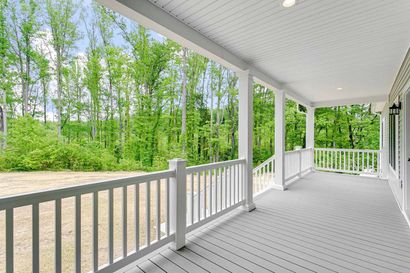 A large porch with a white railing and trees in the background.