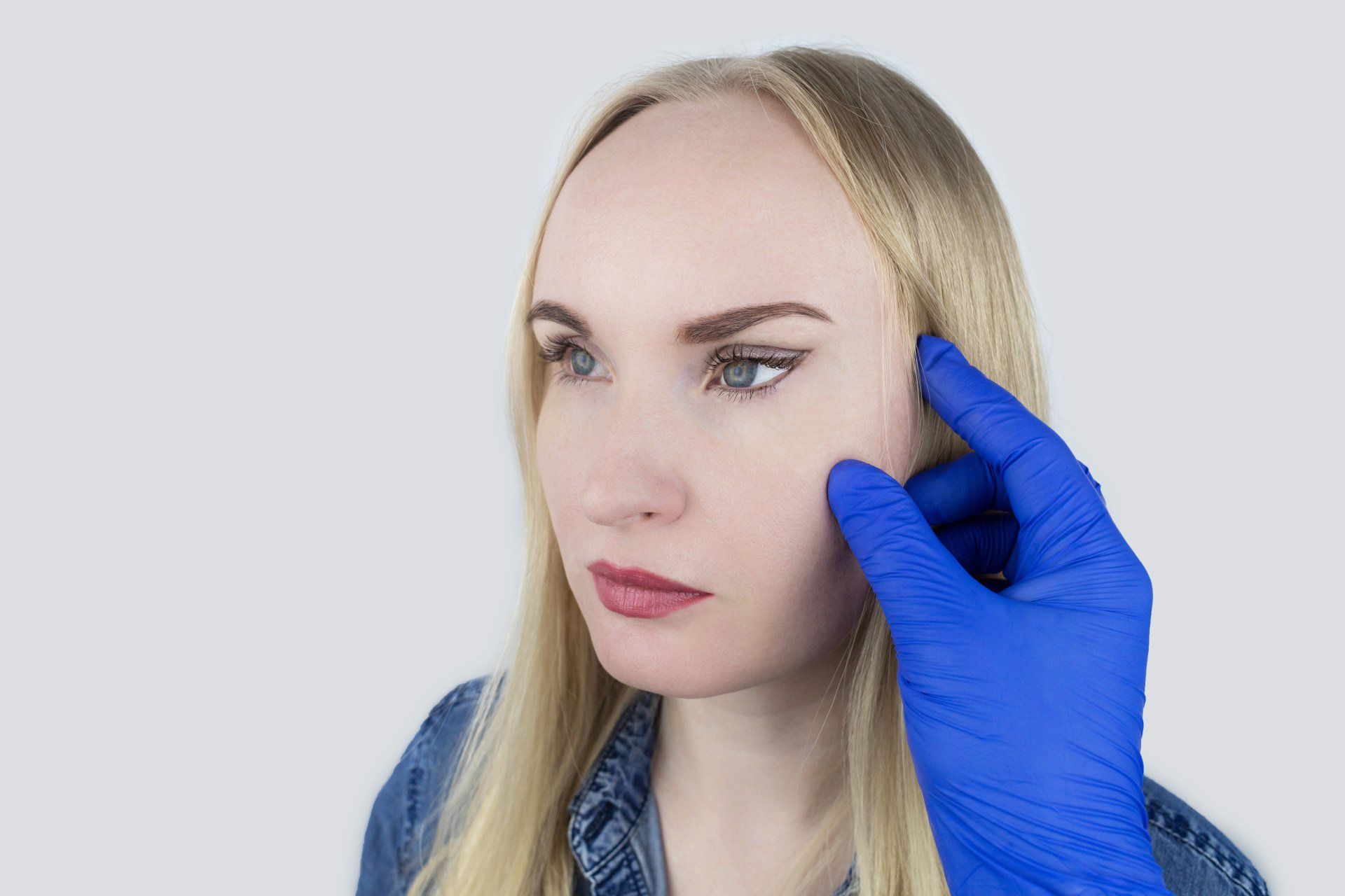 Blonde woman after Fox-Eye lift with gloved hand touching face