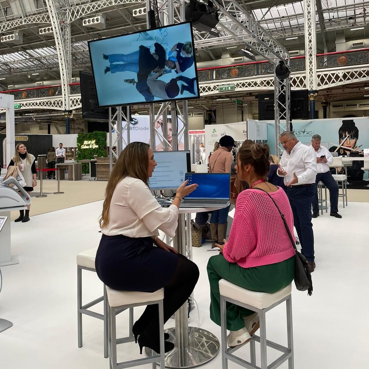 Two women are sitting at a table in front of a large screen.