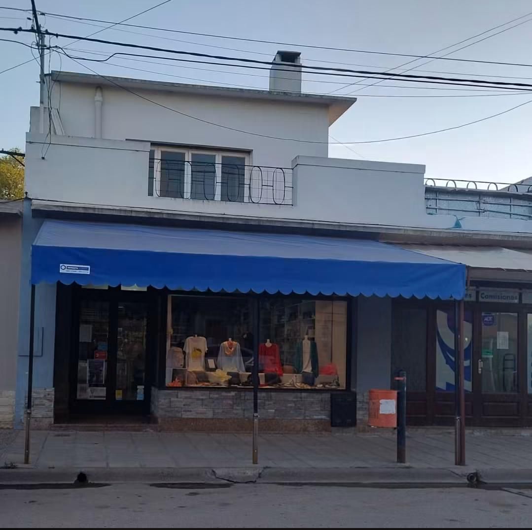 Local comercial a pie de calle con toldo azul y maniquíes en el escaparate, situado debajo de un edificio blanco