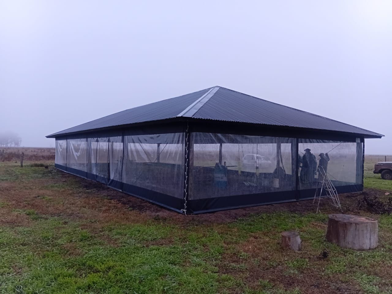 Pabellón negro con forma de tienda de campaña y paredes de plástico transparente en un campo cubierto de niebla.
