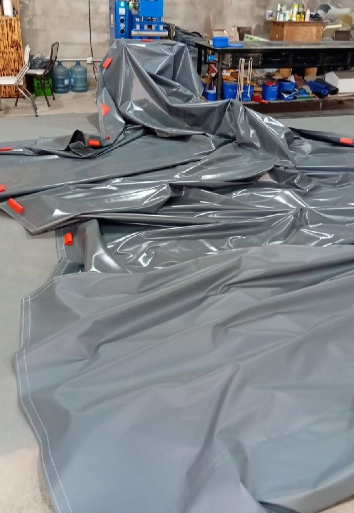 Una lona gris se extiende sobre el suelo de un taller, con herramientas y estanterías de almacenamiento al fondo.