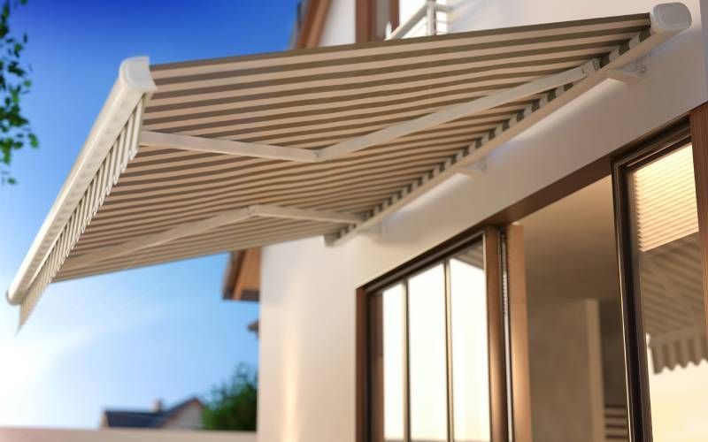 Un toldo retráctil blanco se extiende sobre las ventanas de un edificio moderno contra un cielo azul.