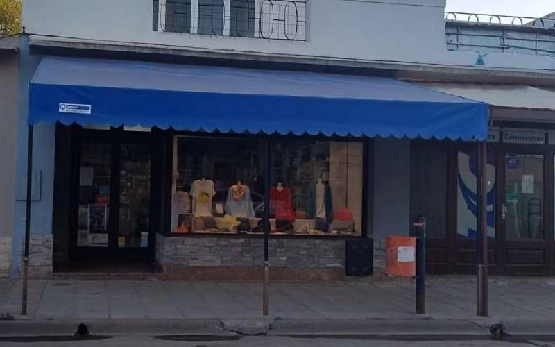 Escaparate con toldo azul y maniquíes en la ventana, detrás de la acera.