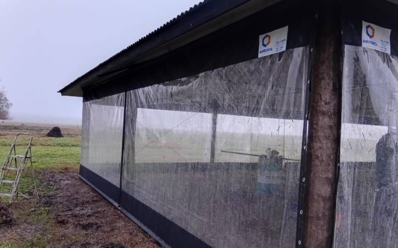Un cobertizo largo y abierto por los lados, con paredes de malla, en un campo de cultivo lluvioso.
