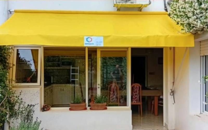 Toldo amarillo sobre un escaparate con grandes ventanales y una pequeña zona de estar al aire libre.