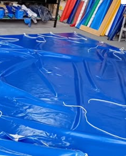 Lona azul o lámina de vinilo extendida en el suelo de una tienda, con rollos de tela de colores al fondo.