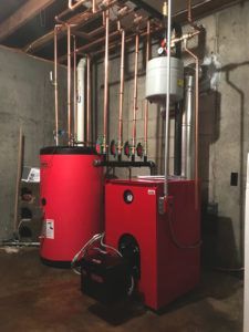 Red heating system with copper pipes and a silver expansion tank in a basement.