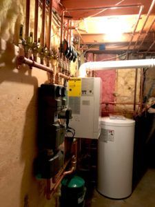 Basement with heating system components, including a white boiler, water tank, and copper pipes.
