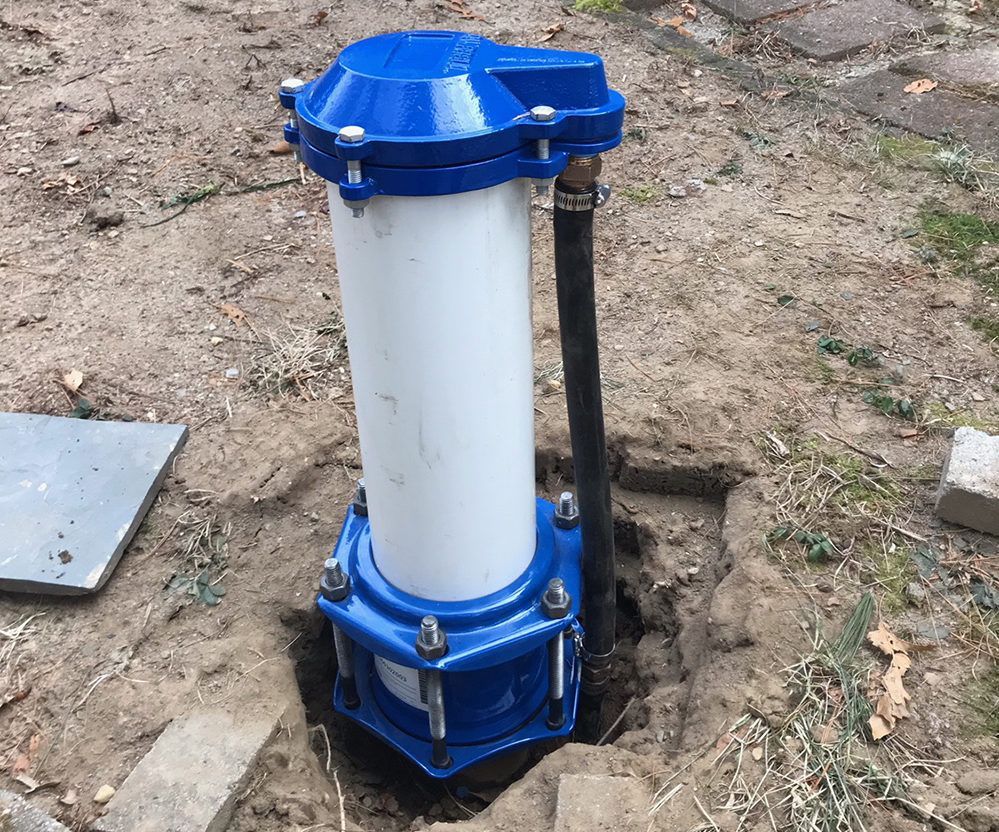 Blue and white wellhead casing with a black pipe extending from the ground.