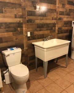 Bathroom with white toilet, utility sink, and wood-paneled walls.