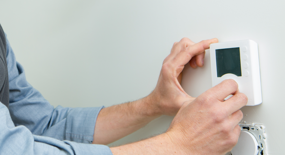 Person adjusting a white thermostat on a white wall.