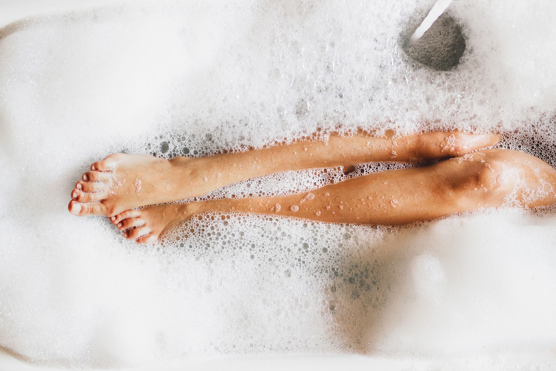 Legs and feet of a person in a bubble bath, soaking. Red toenails.