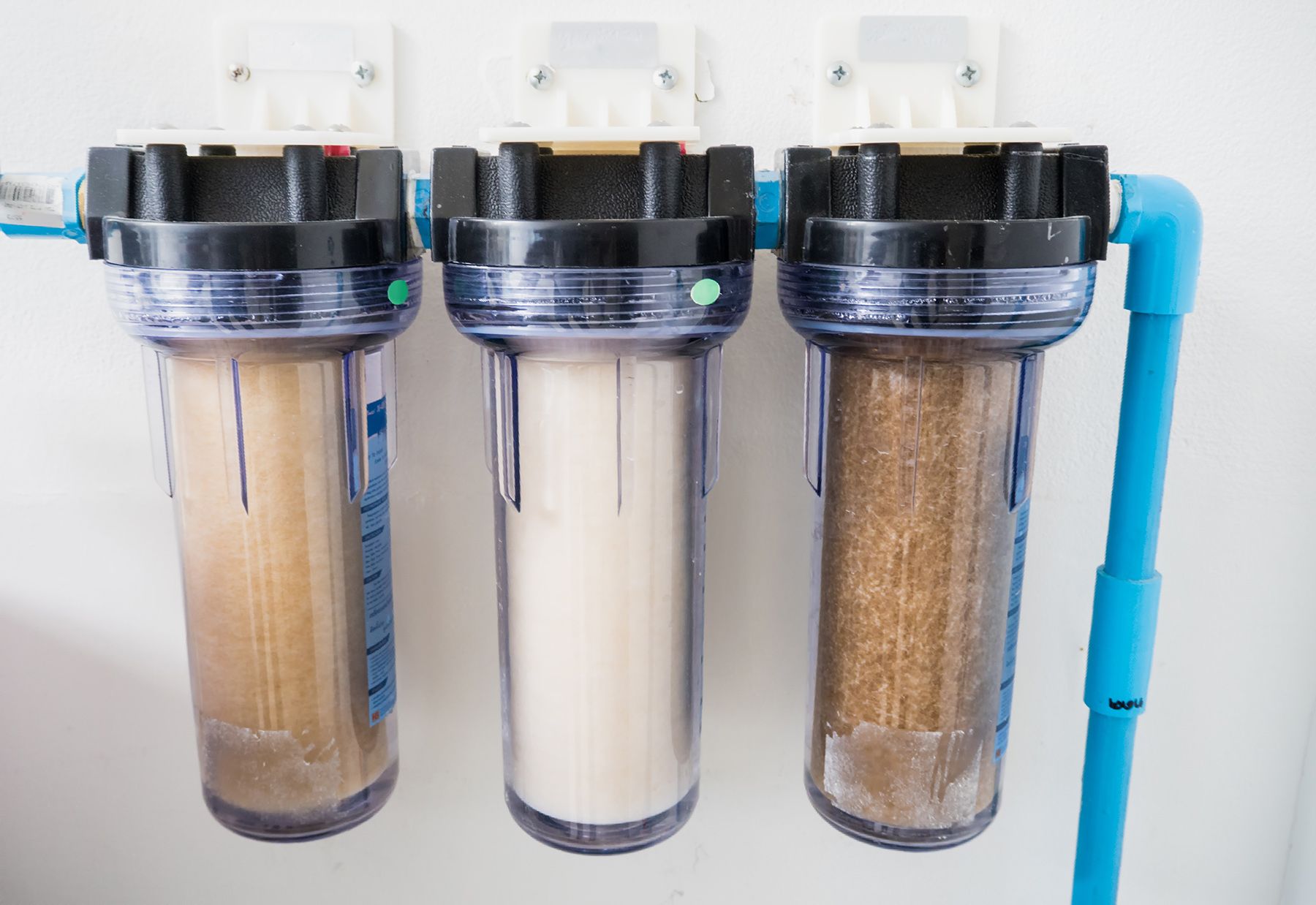 Three clear water filter canisters attached to blue pipes, filled with varying brown and white filter media.