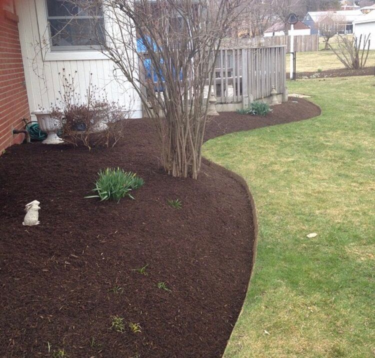 Lawn with freshly mulched garden bed along a house, with green grass and a small deck in the background.