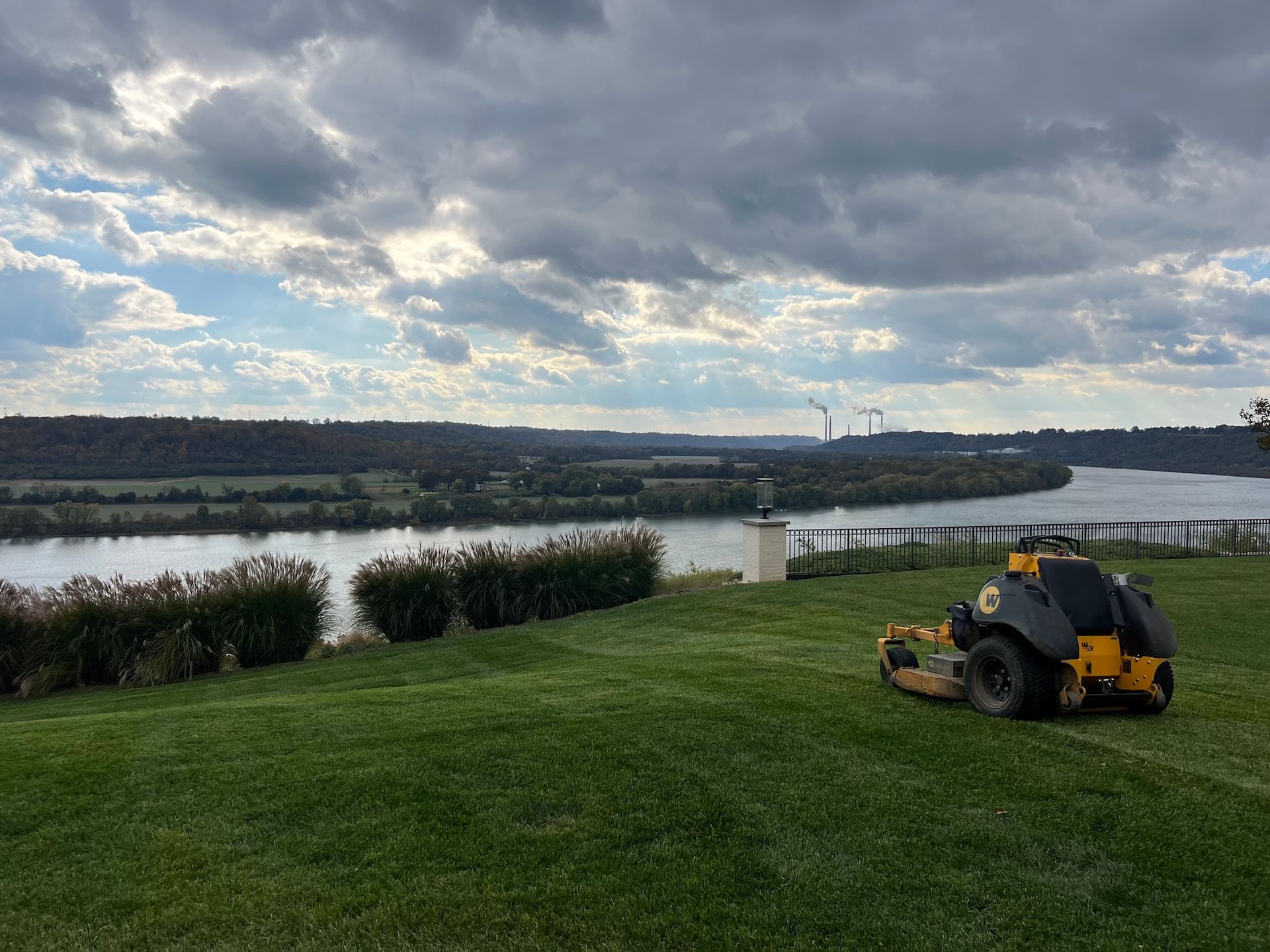A commercial mower on a grassy hill overlooking a river and cloudy sky.