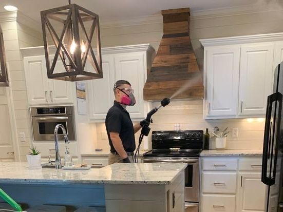 Person spraying a kitchen with a nozzle, wearing a mask, near cabinets and a range.