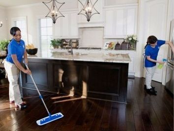 Two people cleaning a kitchen; one mopping, the other wiping the refrigerator.