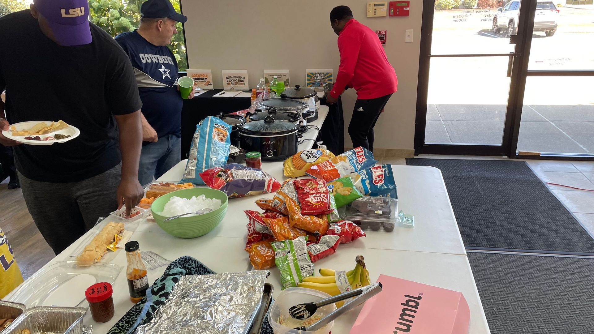 Indoor snack table with chips, bowls, drinks, and people standing nearby by a doorway