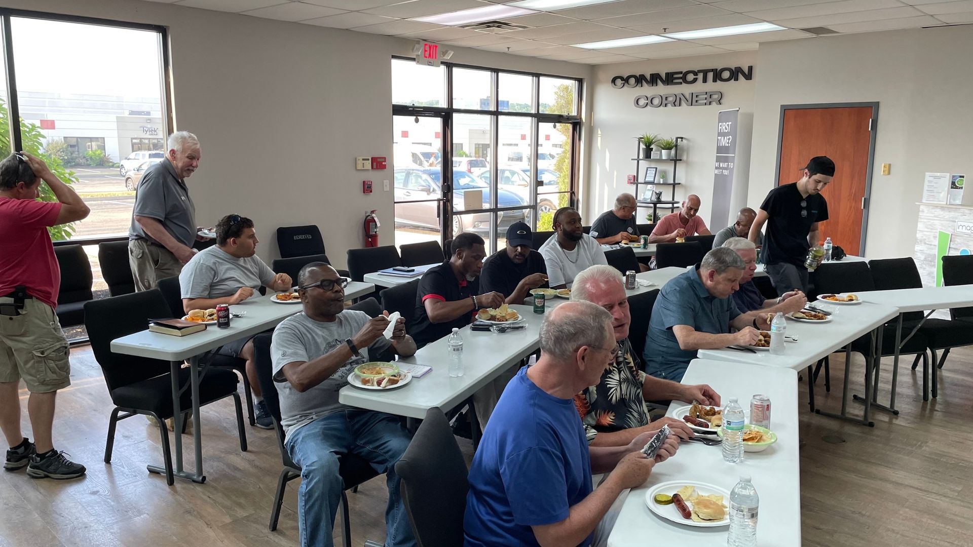People seated at tables in a bright community dining hall, eating and chatting.