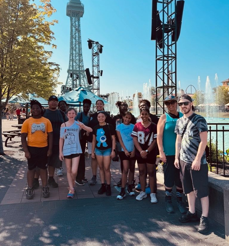 Group posing outdoors at an amusement park near a fountain and tower ride on a sunny day
