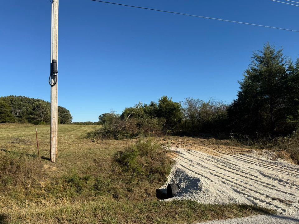 A rural scene with a utility pole, a culvert, and a cleared dirt area under a blue sky.