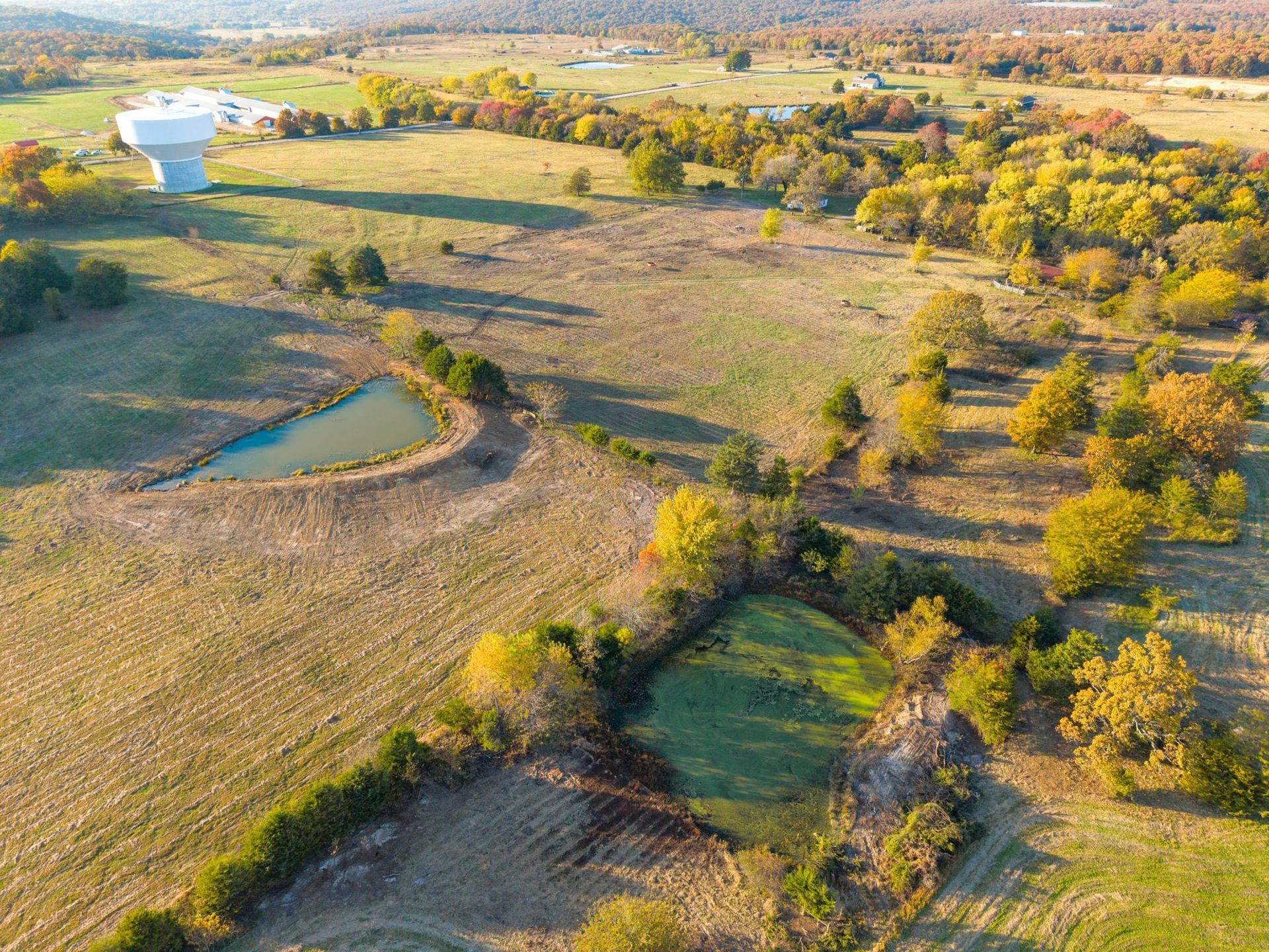 Aerial view of a rural landscape with a pond, trees, and water tower. Autumn colors.