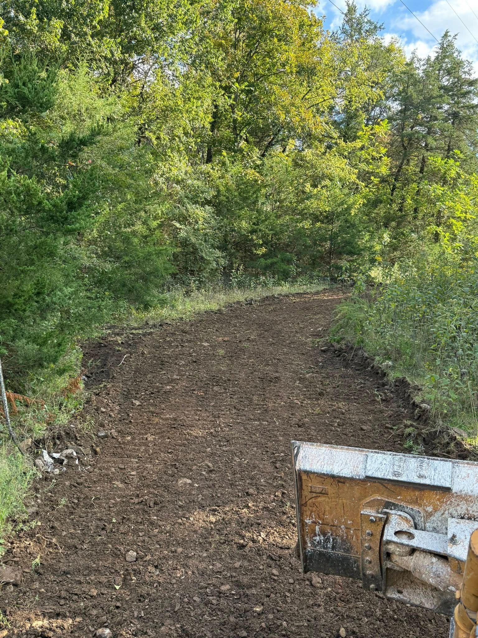 A pile of dirt and a bulldozer blade at a construction site with green trees in the background.