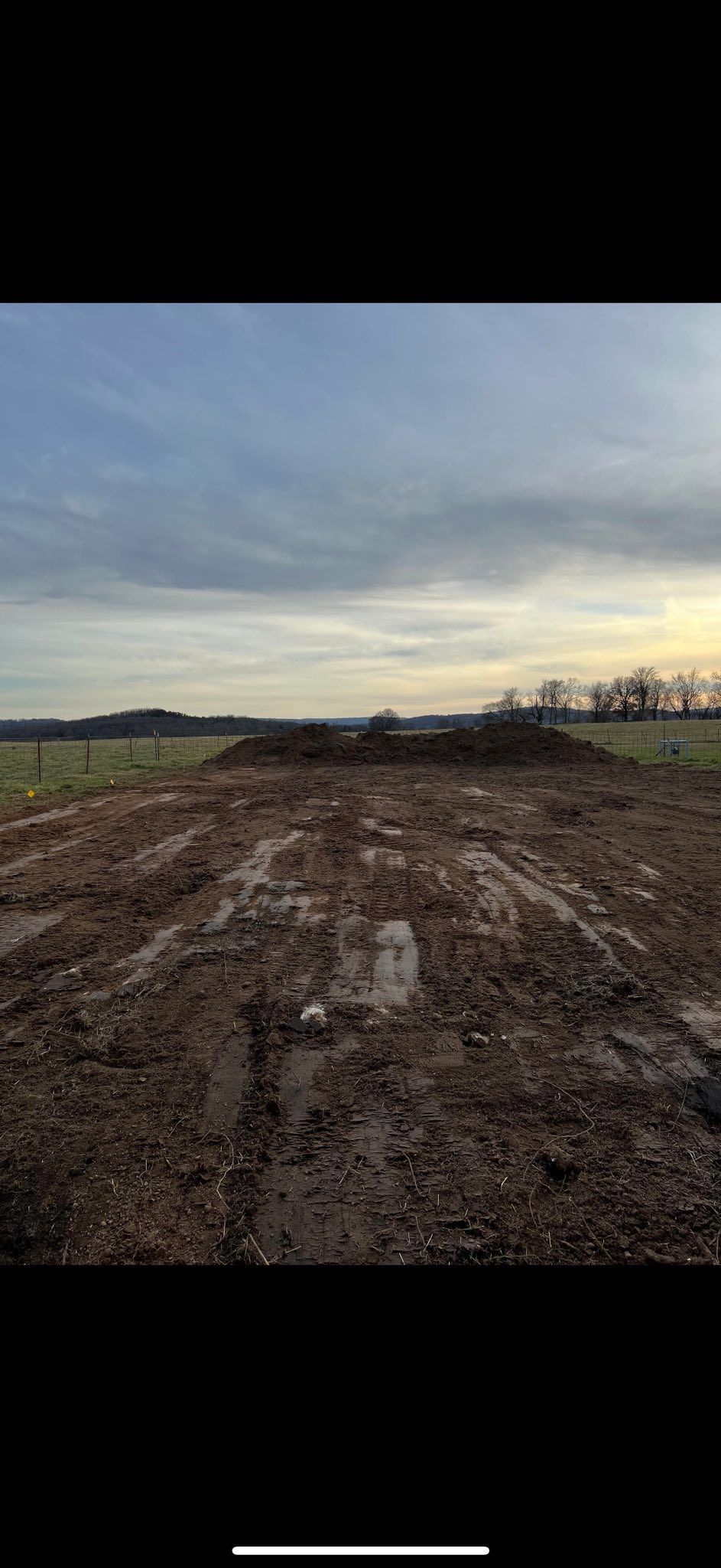 Muddy dirt path leading toward treeline and overcast sky.