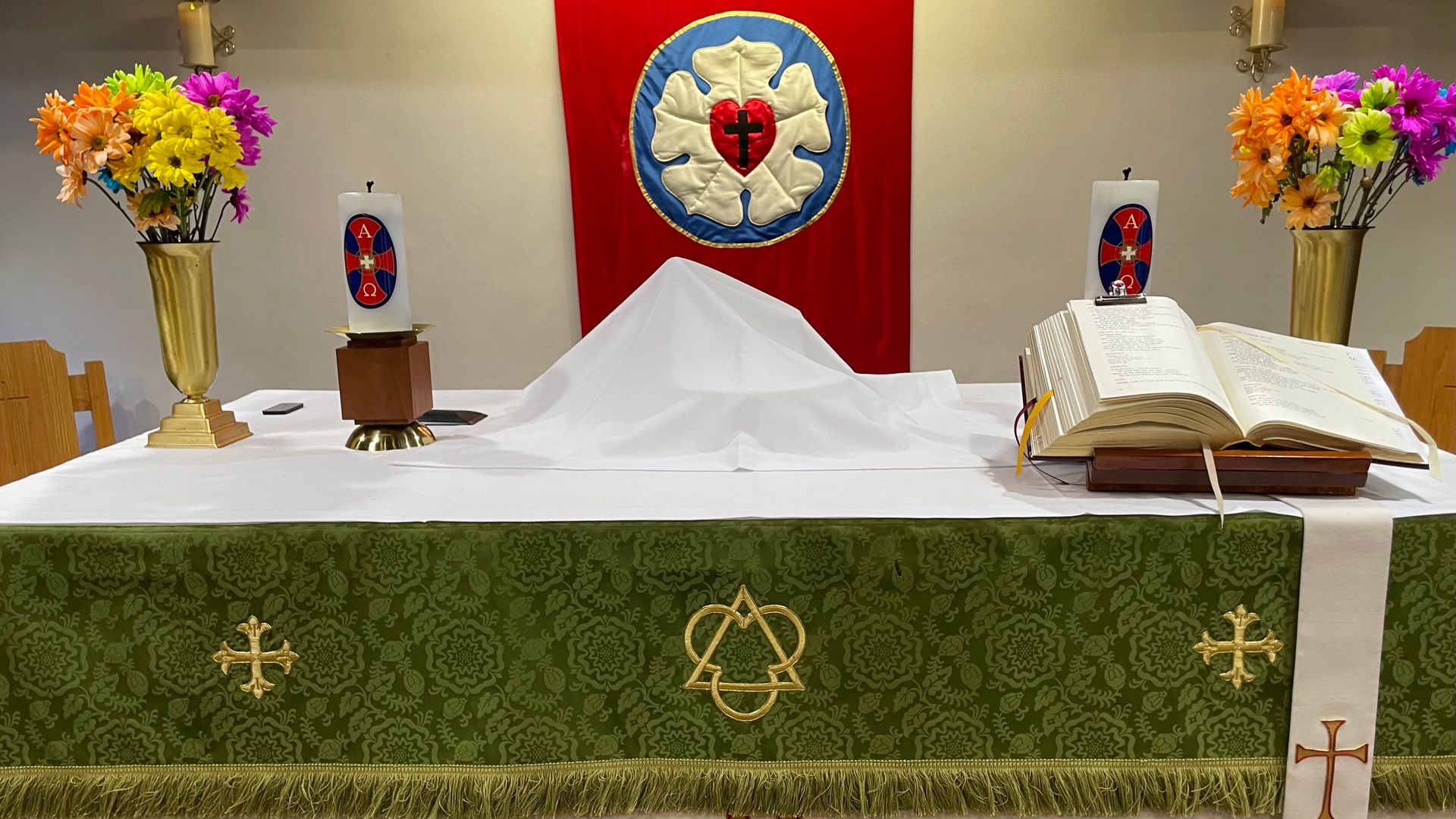 A church altar with a bible , candles , and flowers.