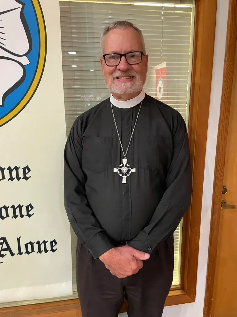 pastor in a black shirt with a silver cross necklace
