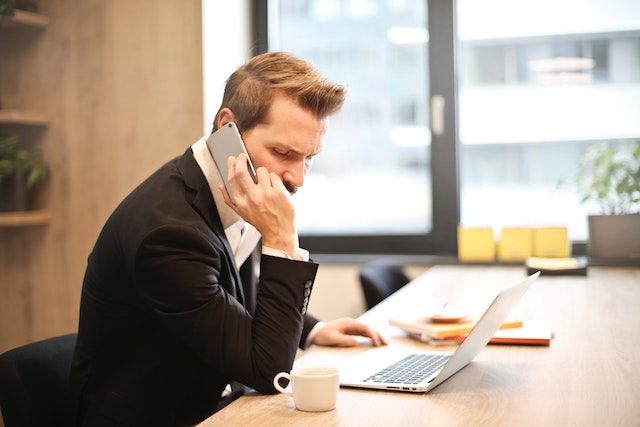 A property manager in a black suit sits at their desk and arranges repair services on their laptop