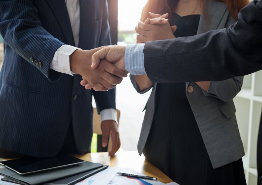 A landlord and property manager, both in black suits, shake hands as they enter into partnership.