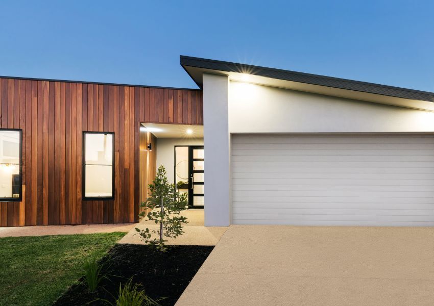 The well lit exterior of a modern single family home is pictured under an evening sky.