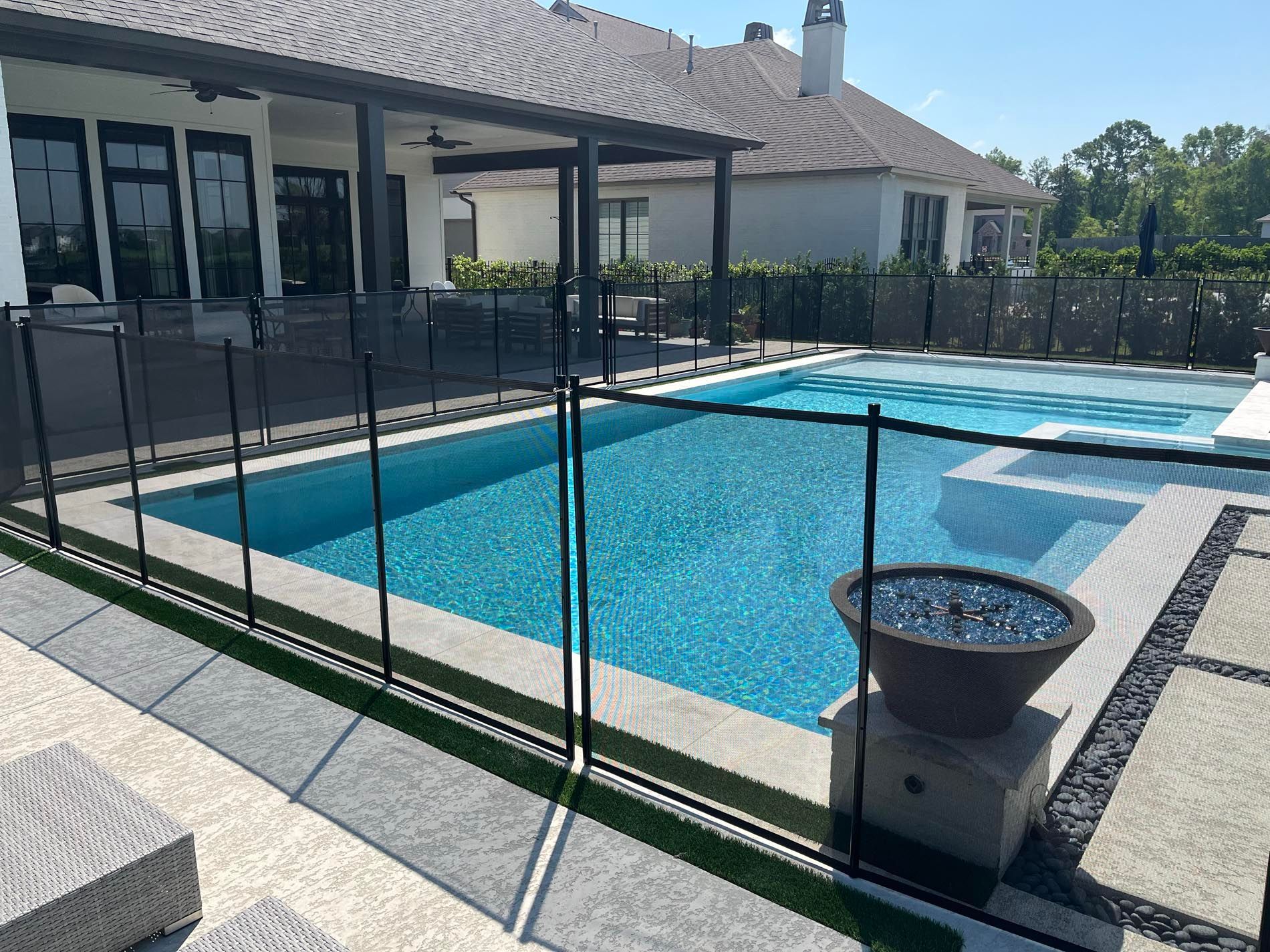 A large swimming pool surrounded by a glass fence in front of a house.