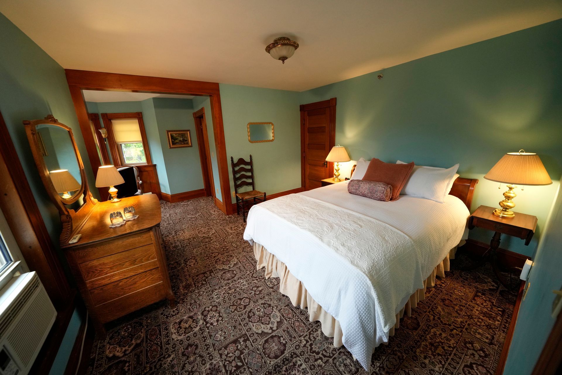 A bedroom with a king size bed , dresser , mirror and lamp.
