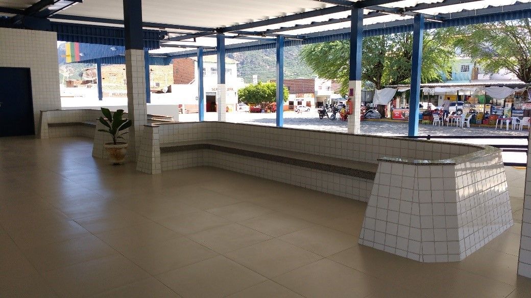 Táxis brancos enfileirados sob a cobertura de um prédio; plantas verdes e um céu azul se destacam.