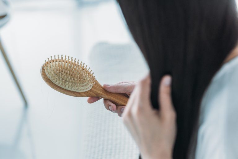 A woman is brushing her hair with a wooden brush.