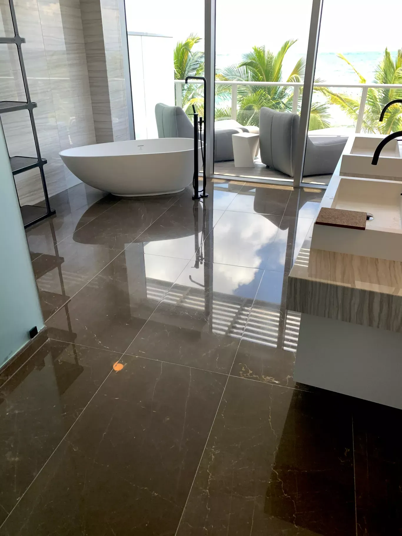 Modern bathroom with glossy dark tile, freestanding tub, and a window seat overlooking greenery.